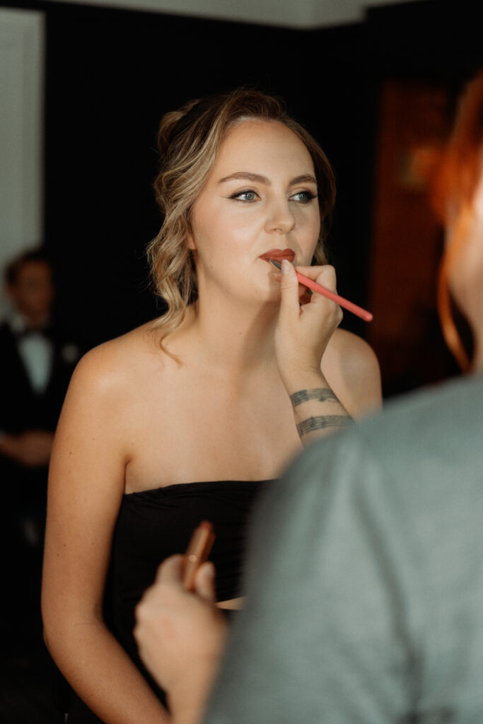 makeup artist applying lipstick to a bride who wants a bold lip